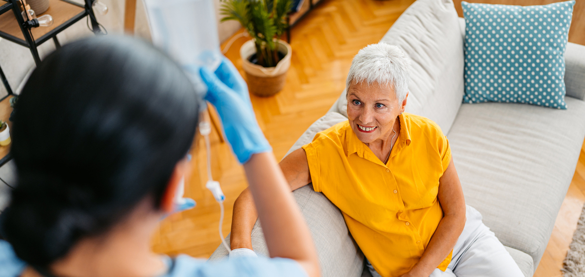 Home care nurse visiting a senior woman at her home. Adjusting IV drip to her patient.